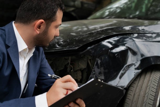 Estimator / claims adjustor examining a car that has been in an accident. Illustrating our claims page